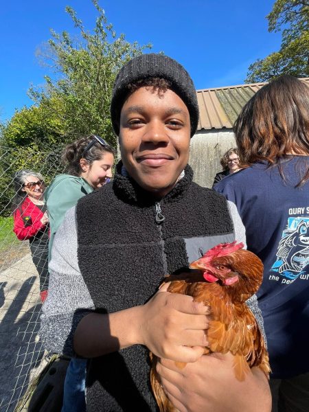 Man wearing a black hat and vest smiles while holding a brown chicken